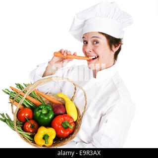 Happy female chef holding a basket of fresh, organic, locally grown produce and eating a raw carrot.  Isolated on white backgrou Stock Photo
