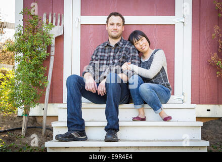 Happy Mixed Race Couple Relaxing on the Steps of Their Barn. Stock Photo