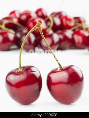 two red cherries and pile of cherry as background on white Stock Photo