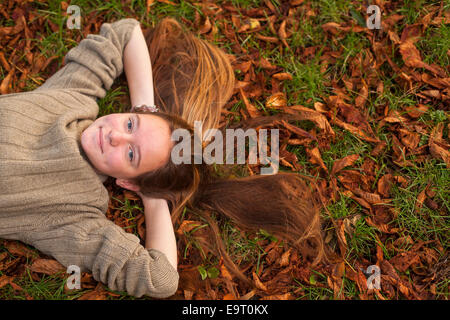 Young pretty girl lying on the ground with fallen leaves in autumn park. Stock Photo