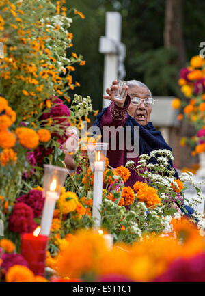 An elderly woman toasts her deceased husband with a shot of mescal at Xoxocatian cemetery decorated with flowers and candles for the Day of the Dead Festival known in spanish as D’a de Muertos on October 31, 2014 in Oaxaca, Mexico. Stock Photo