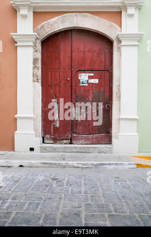 Close-up of large arched red wooden door with a smaller door cut into it on an orange Spanish colonial house, Campeche, Mexico Stock Photo