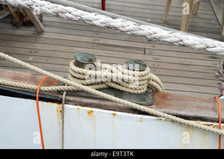 Rope coiled around mooring bollard in harbour with boat deck behind Stock Photo