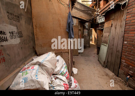 A cluttered hutong alleyway with cement sacks, wooden doors and hanging laundry, Beijing, China Stock Photo