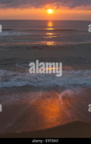 Scenic shot of the dark, restless sea and clouds reflecting on the wet sand at dusk Stock Photo