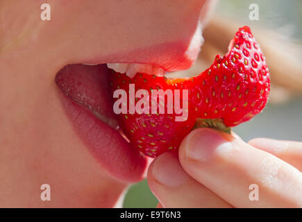 Close Up of a Young Woman's mouth biting into a ripe strawberry
