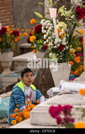 Oaxaca, Oaxaca, Mexico. 31st Oct, 2014. A young boy at the tomb of his grandfather at Xoxocatian cemetery decorated with flowers and candles for the Day of the Dead Festival known in spanish as D'a de Muertos on October 31, 2014 in Oaxaca, Mexico. © Richard Ellis/ZUMA Wire/Alamy Live News Stock Photo