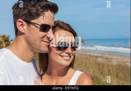 Portrait of a man and woman romantic couple in white clothes wearing sunglasses on a beach with bright clear blue sky Stock Photo