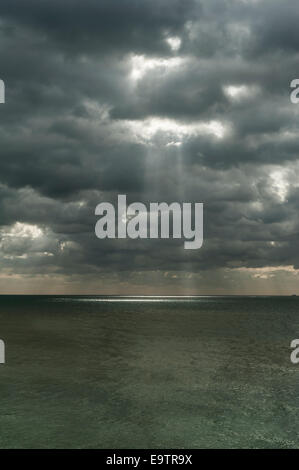 Sun rays bursting through a stormy cloudy sky over the sea in the UK Stock Photo