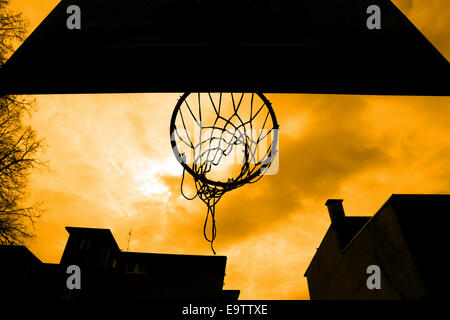 A silhouette of a basketball hoop at playground, taken from below with yellow sky. Stock Photo