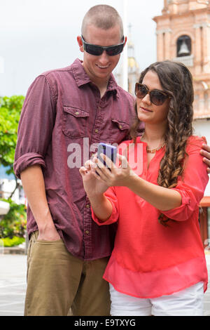 Young couple checking smartphone while walking in the city of Puerto Vallarta, Mexico. Stock Photo