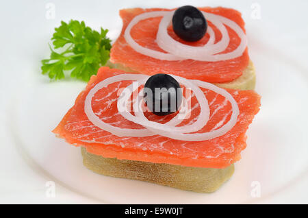 salmon sandwiches with black olives, onion rings and parsley on white plate, close up Stock Photo