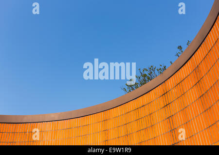 View up at a curved vibrant orange tiled wall set against the deep blue sky in Berlin, Germany. Stock Photo