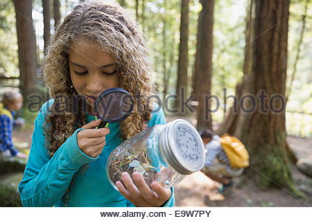 Girl with magnifying glass examining plants in jar