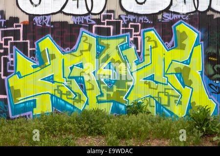 A chartreuse green graffiti tag on a corrugated steel wall at ground level with weeds in the foreground. Stock Photo