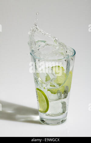 Ice cubes falling into a glass with water and lime Stock Photo