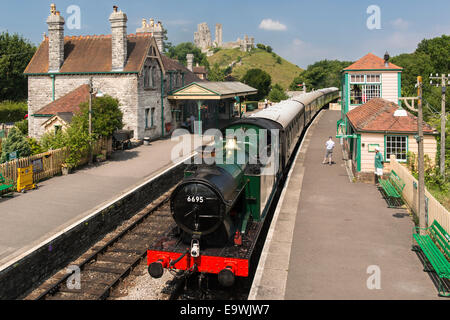 High angle view of steam engine train arriving at Corfe Castle station on the heritage Swanage Railway. Castle ruins in shot. Stock Photo