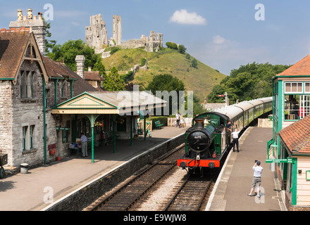 High angle view of steam engine train arriving at Corfe Castle station on the heritage Swanage Railway. Castle ruins in shot. Stock Photo