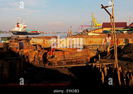 Workers unloading sands from a barge as a cargo ship moving on river Musi in the background in Palembang, South Sumatra, Indonesia. Stock Photo