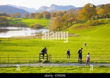 Tourists stepping over a style alongside a footpath at Loughrigg Tarn, The Lake District, Cumbria, England, UK. Stock Photo