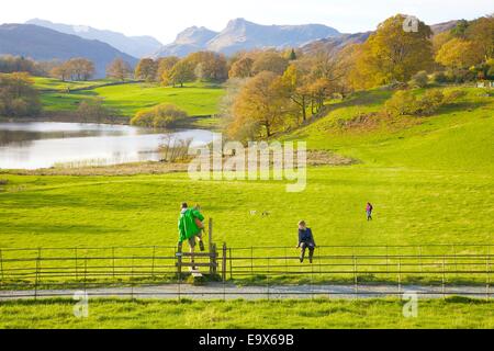 Tourists stepping over a style holding a dog alongside a footpath at Loughrigg Tarn, The Lake District, Cumbria, England, UK. Stock Photo