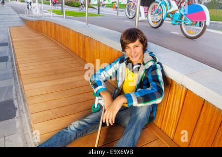 Smiling boy sits with arm on knee holds skateboard Stock Photo
