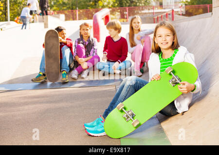 Kids sit behind and girl in front with skateboard Stock Photo