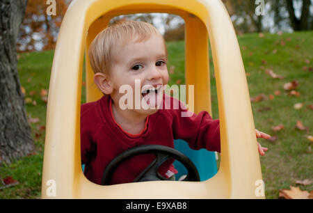 A toddler makes a happy face while playing in his toy car in autumn. Stock Photo