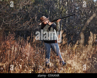 Waterfowl hunting, the female hunter use the shotgun, autumnal bushes on background Stock Photo