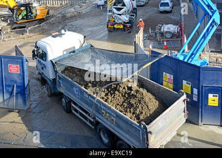 Tipper truck driver using mirrors reversing from building site dust net covering & locating over excavated earth (banksman out of shot)  Southwark UK Stock Photo