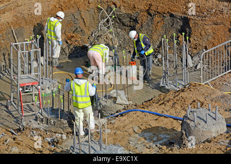 Group workmen cutting back & cleaning up concrete pile tops preparing foundations yellow safety caps fitted  on steel bars Southwark South London UK Stock Photo