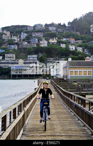 lady with helmet rides rental bike on old wooden pier in Sausalito California Stock Photo