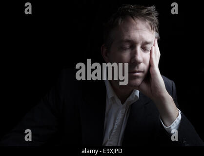 Portrait of businessman closing eyes while working late at night on black background with copy space Stock Photo