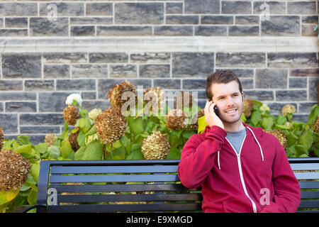 A man sitting on a bench outside using his phone Stock Photo