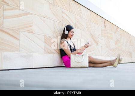 A young woman relaxing using a smartphone with headphones Stock Photo