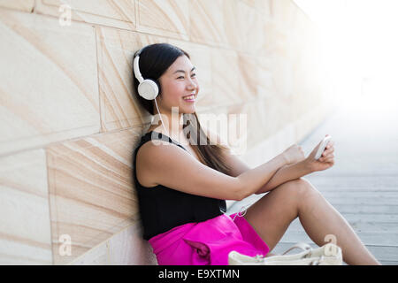 A young woman relaxing using a smartphone with headphones Stock Photo