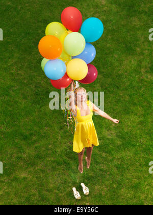Young happy woman flying up from the ground on colorful air balloons Stock Photo
