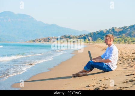 handsome young man with a laptop sitting on the beach Stock Photo