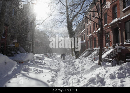 Two people walking up a street blocked with snow after a heavy winter storm in Brooklyn New York Stock Photo
