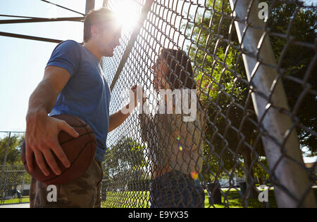 Young couple with basketball standing by wire fence Stock Photo