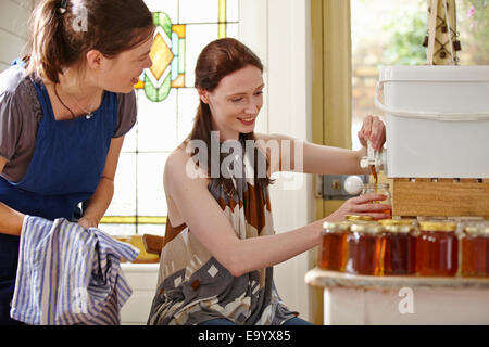 Female beekeepers in kitchen, bottling filtered honey from beehive Stock Photo
