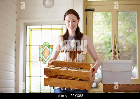 Female beekeeper in kitchen carrying a crate of honey jars from beehive Stock Photo