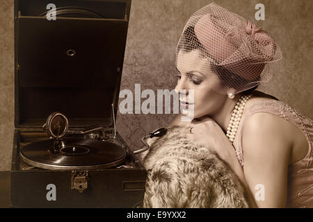 Vintage 1920s style lady in pink listening to an antique record player Stock Photo