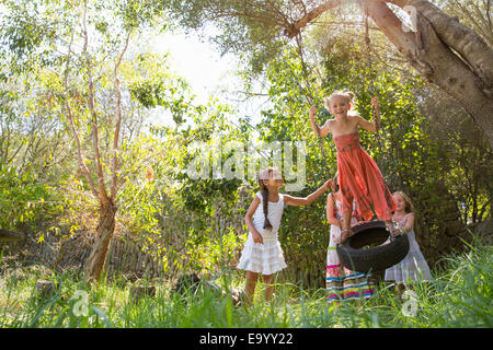 Four girls playing on tree tire swing in garden Stock Photo