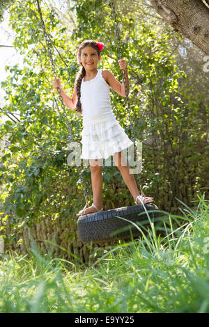 Girl standing swinging on tree tire swing in garden Stock Photo