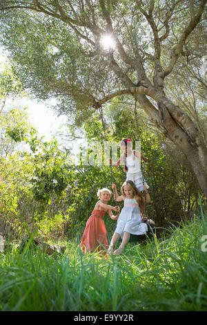 Three girls playing on tree tire swing in garden Stock Photo