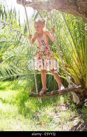 Girl standing swinging on tree swing in garden Stock Photo