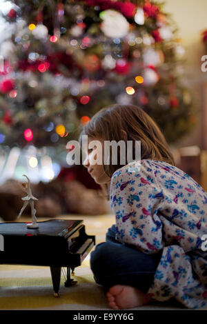 Girl sitting on living room floor listening to toy piano music box at Xmas Stock Photo