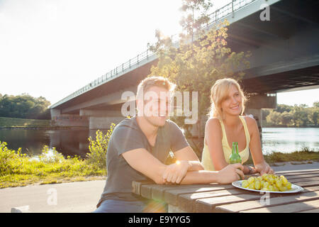 Young couple drinking beer on riverside picnic bench Stock Photo