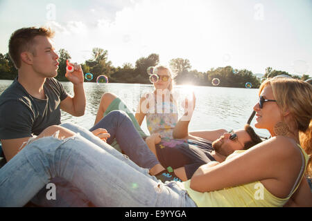 Four young adult friends blowing bubbles on riverside pier Stock Photo